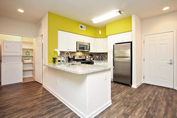 A kitchen with white appliances and a yellow accent wall at The Kitt at Warner Center in Woodland Hills, California, 91303