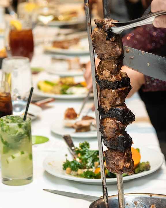 A person is cutting a piece of meat off a skewer.