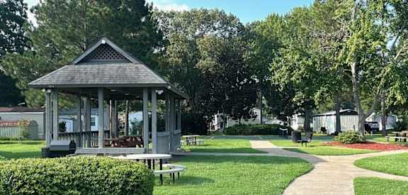 A gazebo is situated in a park with a paved walkway leading to it.