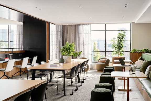 A modern office space with a long table and chairs, a green couch, and a large window with plants.