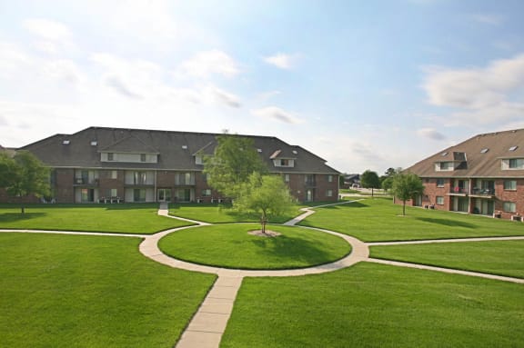 Spacious grounds with walking paths, lush green grass and trees, surrounded by brick apartment buildings at Fountain Glen Apartments in Lincoln, NE.