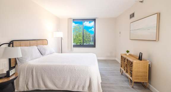 A bedroom with a large bed and a window overlooking a green landscape.
