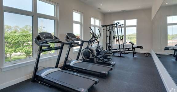 a gym with cardio equipment and large windows