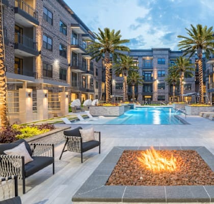 A fire pit sits in the middle of a courtyard surrounded by palm trees and buildings.