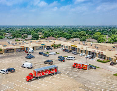 A parking lot with a red truck in the foreground and a shopping center in the background.