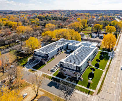 A large building with a grey roof is surrounded by trees with yellow leaves.