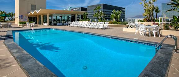 A swimming pool with sun loungers and a building in the background.