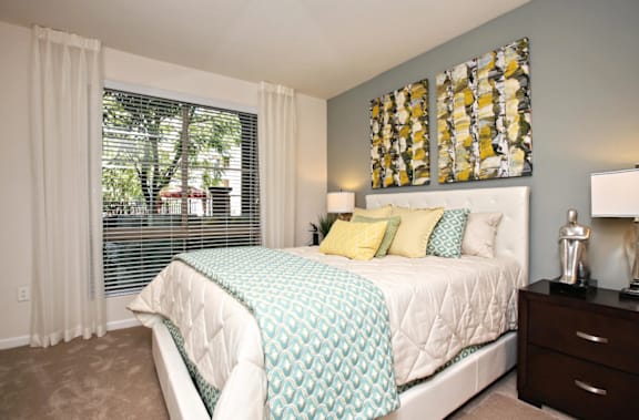 A bedroom with a bed, nightstand, and a window with blinds at The Kitt at Warner Center in Woodland Hills, California