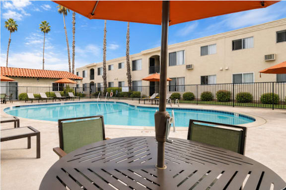 A pool with a table and chairs and an umbrella in the foreground.