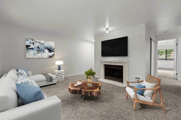 A living room with a grey couch, a wooden coffee table, and a television mounted on the wall  at Brackett Apartments, WA, 98020