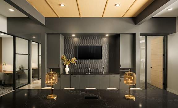 A modern conference room with TV, table, chairs, black countertops and gold accents.