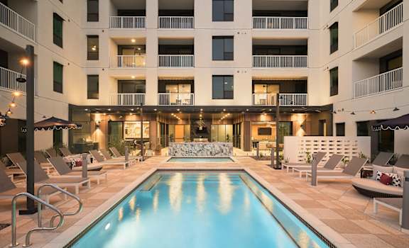 A large swimming pool in front of a building with a patio area.