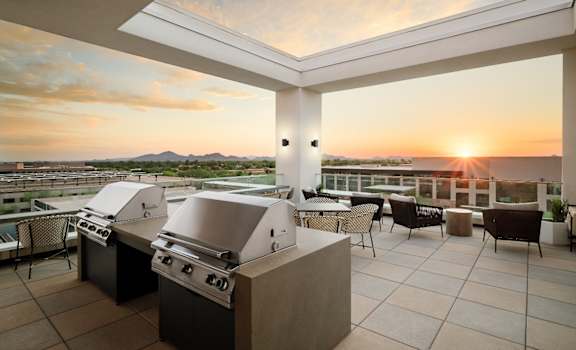 A modern outdoor kitchen with a grill and seating area overlooking a sunset.