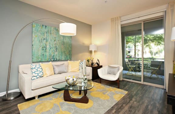 A living room with a white couch, a glass table, and a painting on the wall at The Kitt at Warner Center in Woodland Hills, CA