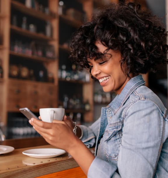 a woman looking at her cell phone while holding a cup of coffee