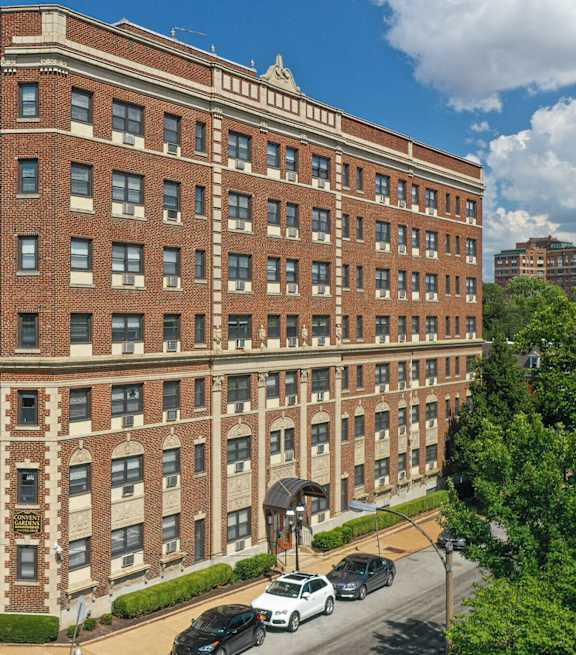 A large red brick building with a white car parked in front.at Convent Gardens Apartments, St. Louis, MO, 63108