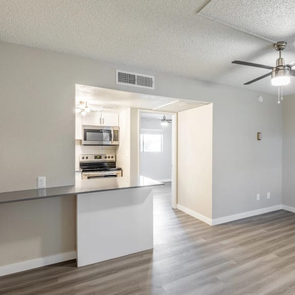 A spacious room with a ceiling fan and a kitchenette in the background.