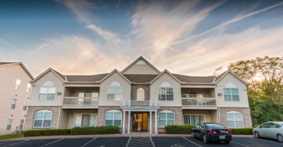 A large, well-lit apartment complex with multiple balconies and cars parked in the driveway.