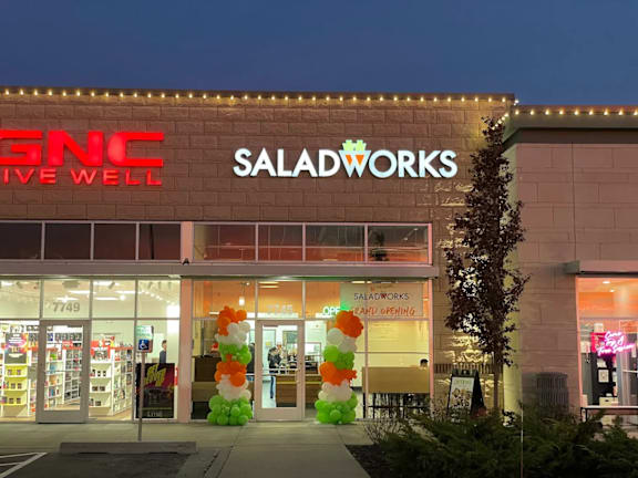 The storefront of a GNC and Saladworks store at night.