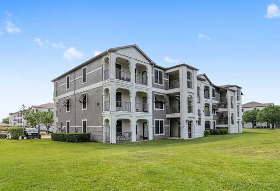 A large, grey apartment building with multiple balconies and doors.