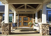 Thumbnail 3 of 6 - A building with a brown door and a white pillow on a bench.