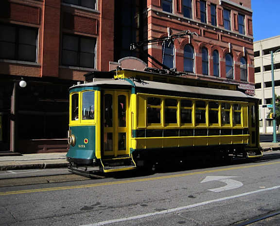A yellow and green streetcar is on a city street.