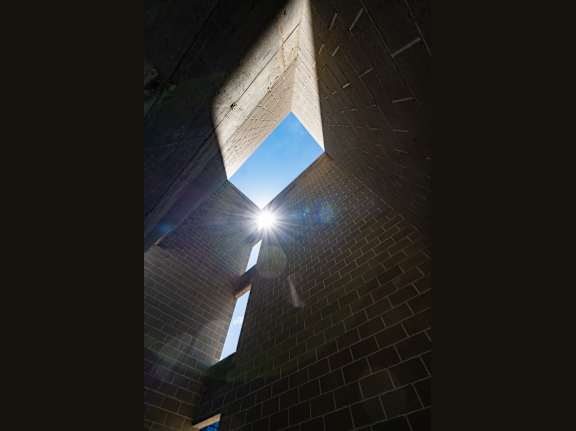 The sun shines through a square window in a dark brick wall.
