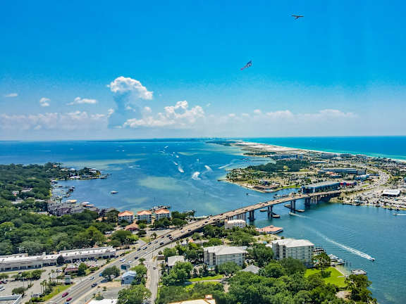A bird flies over a city with a large body of water and a bridge.