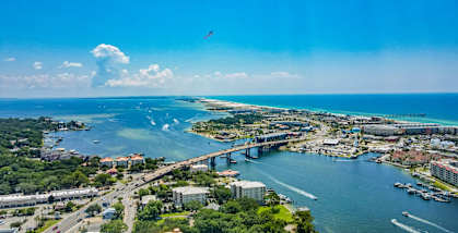 A bird flies over a city with a large body of water and a bridge.
