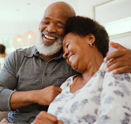 An older couple is sitting together, smiling and laughing.