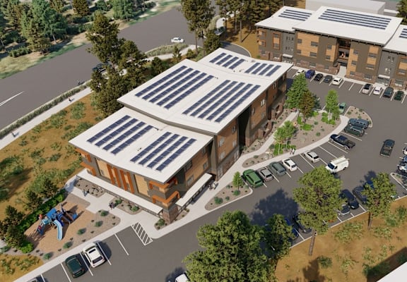 A building with solar panels on the roof is surrounded by a parking lot and trees.