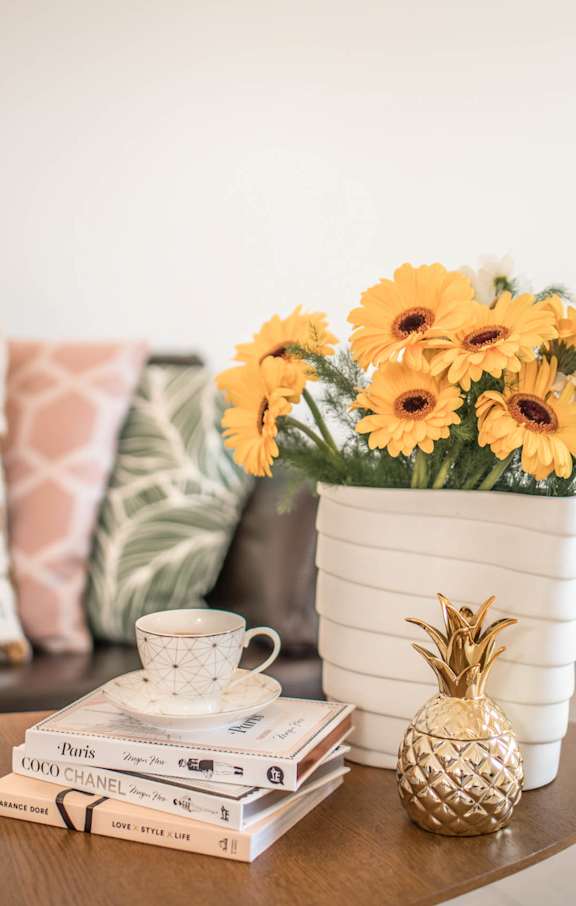 A table with a stack of books, a cup of tea, a pineapple, and a vase of flowers.
