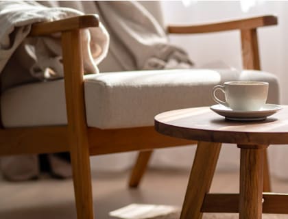 A wooden chair with a cup of coffee on a saucer is placed on a woven rug.