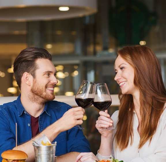 A man and a woman are sitting at a table, sharing a glass of wine.