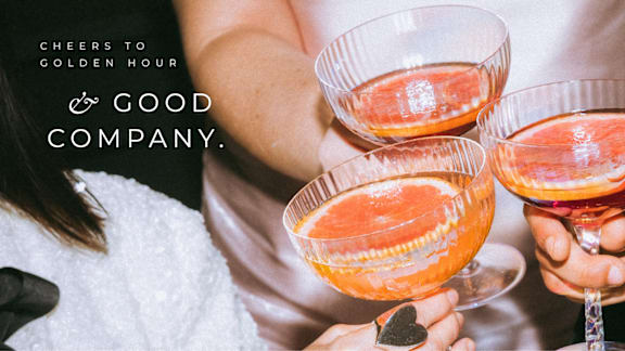 A person is holding two glasses of a pink beverage.