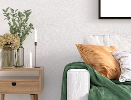 A white couch with a green blanket and a vase with flowers on a wooden table.