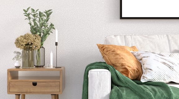 A white couch with a green blanket and a vase with flowers on a wooden table.