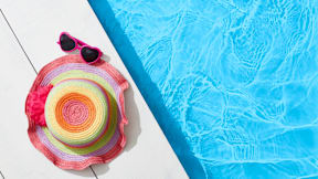 A colorful hat and sunglasses are placed on a white surface next to a blue pool.