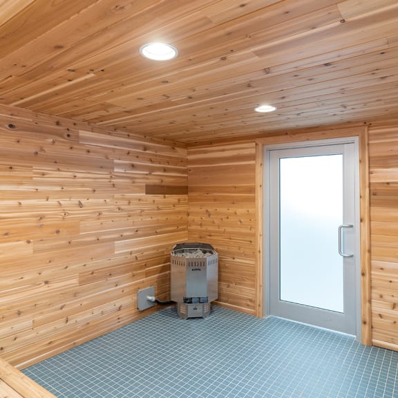 an open door leads into a sauna with wood walls and a blue tiled floor