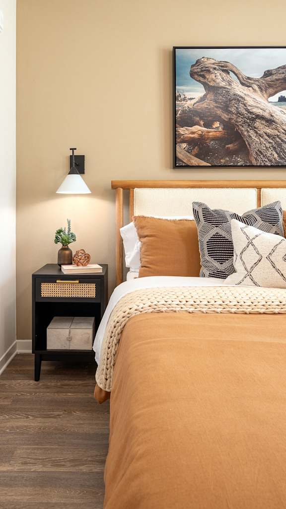 A bedroom with a bed, nightstand, lamp, and a painting on the wall.