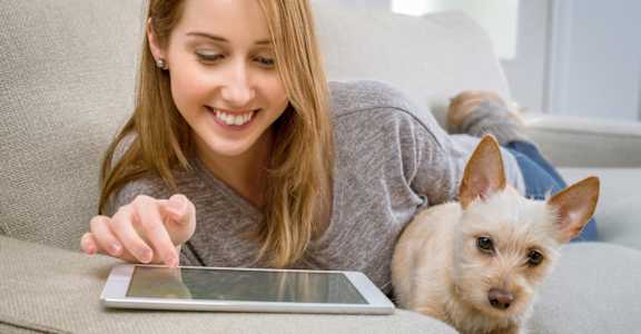 A woman is lying on a couch with a tablet in her hand and a dog beside her. at  The Orleans of Decatur, Georgia