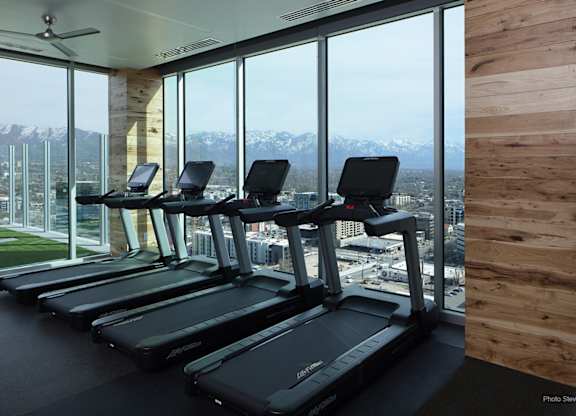A row of treadmills in a gym with a view of the city and mountains outside the window.