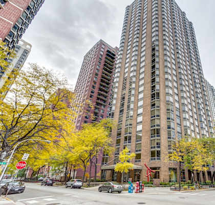 A tall building with a red awning sits in front of a tree with yellow leaves at Elm Street Plaza, Chicago