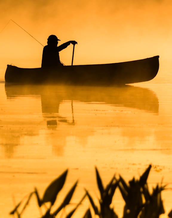 A person is fishing in a canoe on a calm body of water at West Oak Apartments, Wake Forest, NC