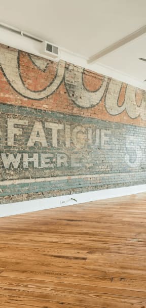 an old mural on a brick wall in an empty room with hardwood floors and a ceiling