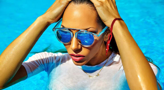 a woman wearing sunglasses in a pool with her hands on her head