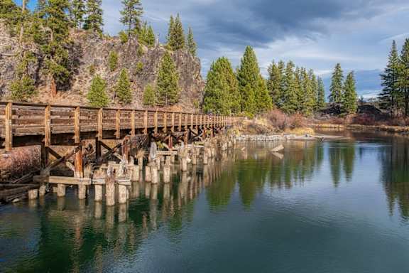 A wooden bridge over a calm body of water with trees in the background.