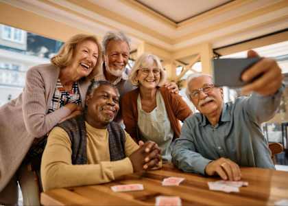 A group of seniors are taking a selfie while playing cards.