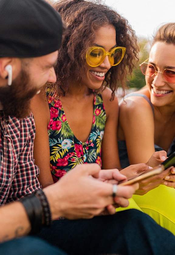 a group of friends sitting on the grass looking at their cell phones