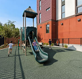 A playground with a green slide and a red building in the background.